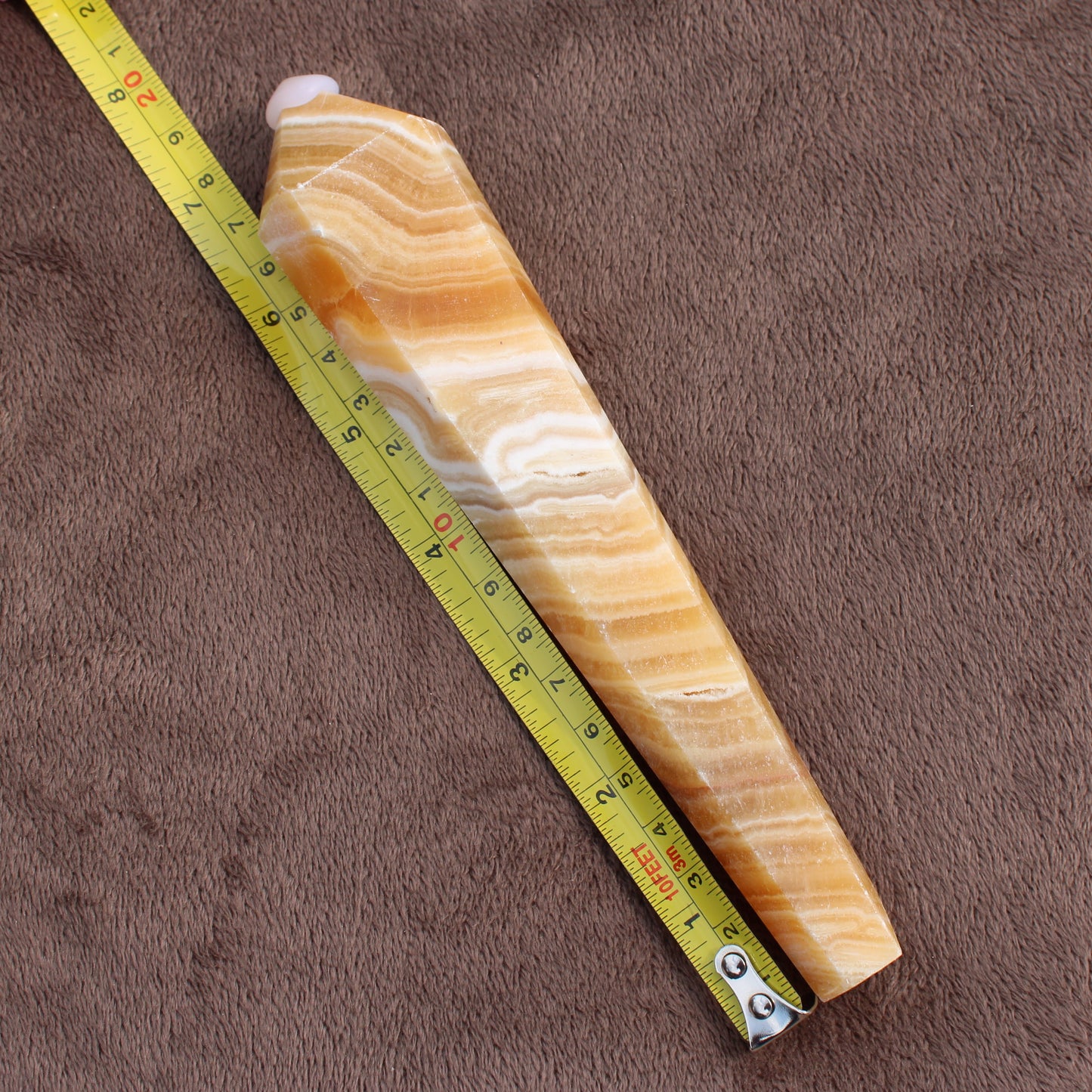 Honey Calcite Wand from Different Branches LLC next to a measuring tape on brown fabric