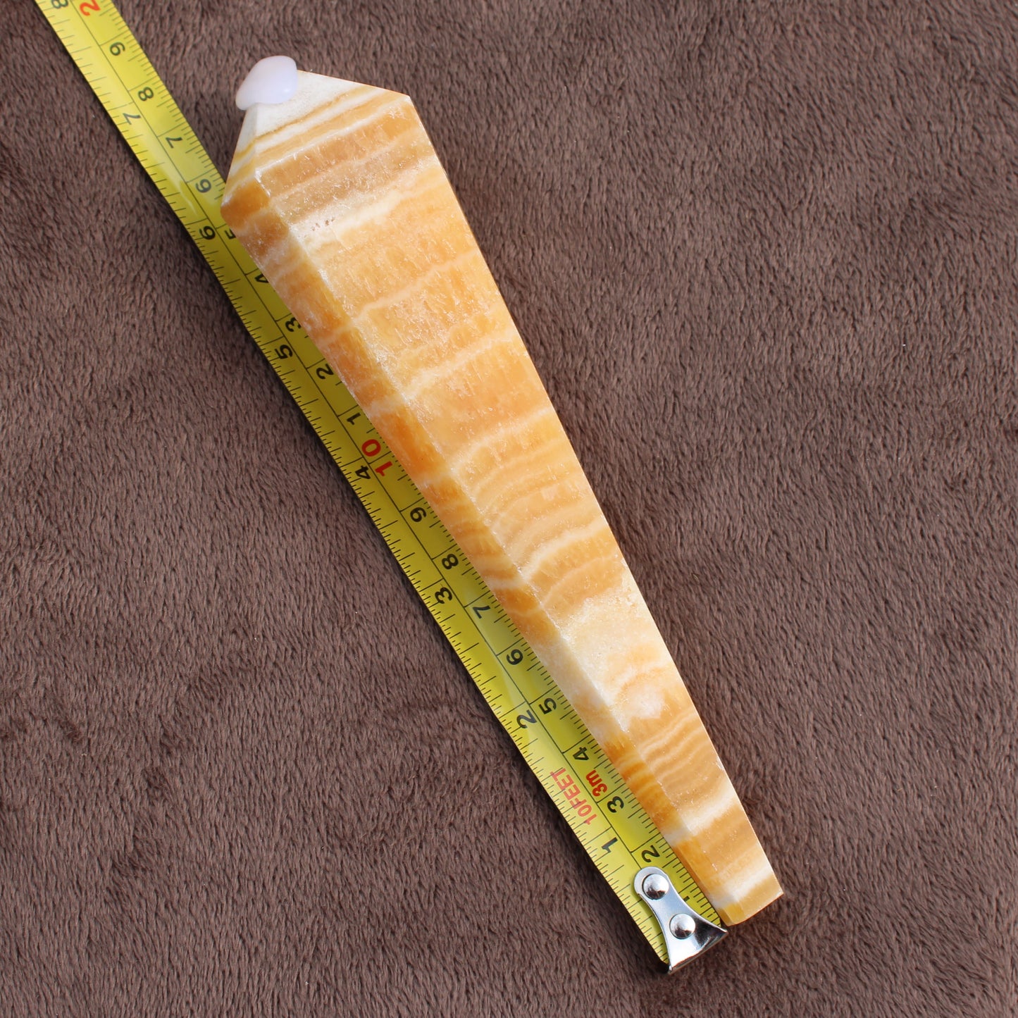Honey Calcite Wand crystal displayed next to measuring tape on brown fabric background