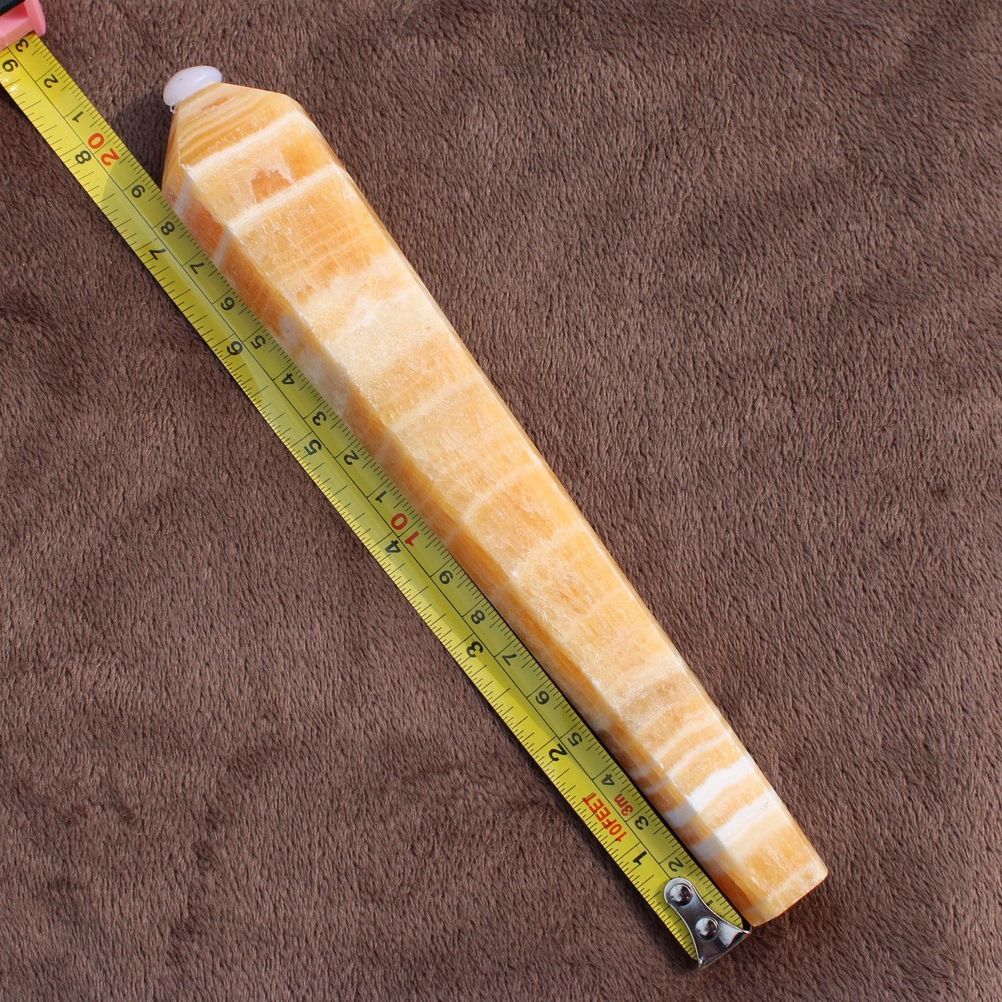 Honey Calcite Wand from Different Branches LLC with yellow and white banding next to measuring tape