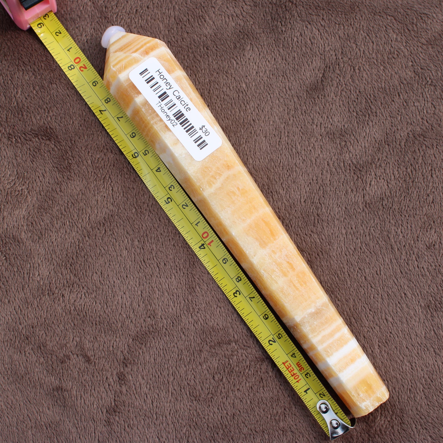 Honey Calcite Wand crystal from Different Branches LLC next to a measuring tape on brown fabric