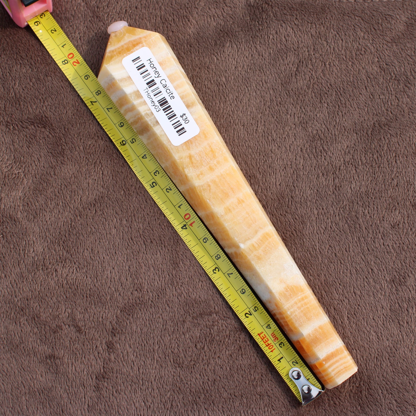 Honey Calcite Wand crystal with natural orange and white banding next to measuring tape on brown background