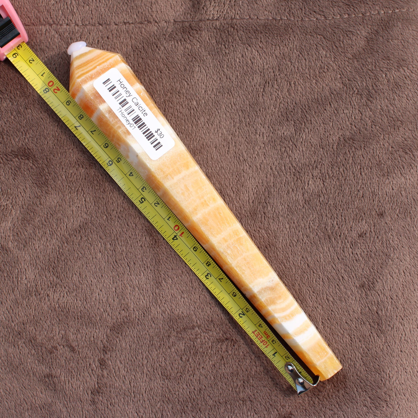 Honey Calcite Wand crystal from Different Branches LLC next to a measuring tape on a brown surface