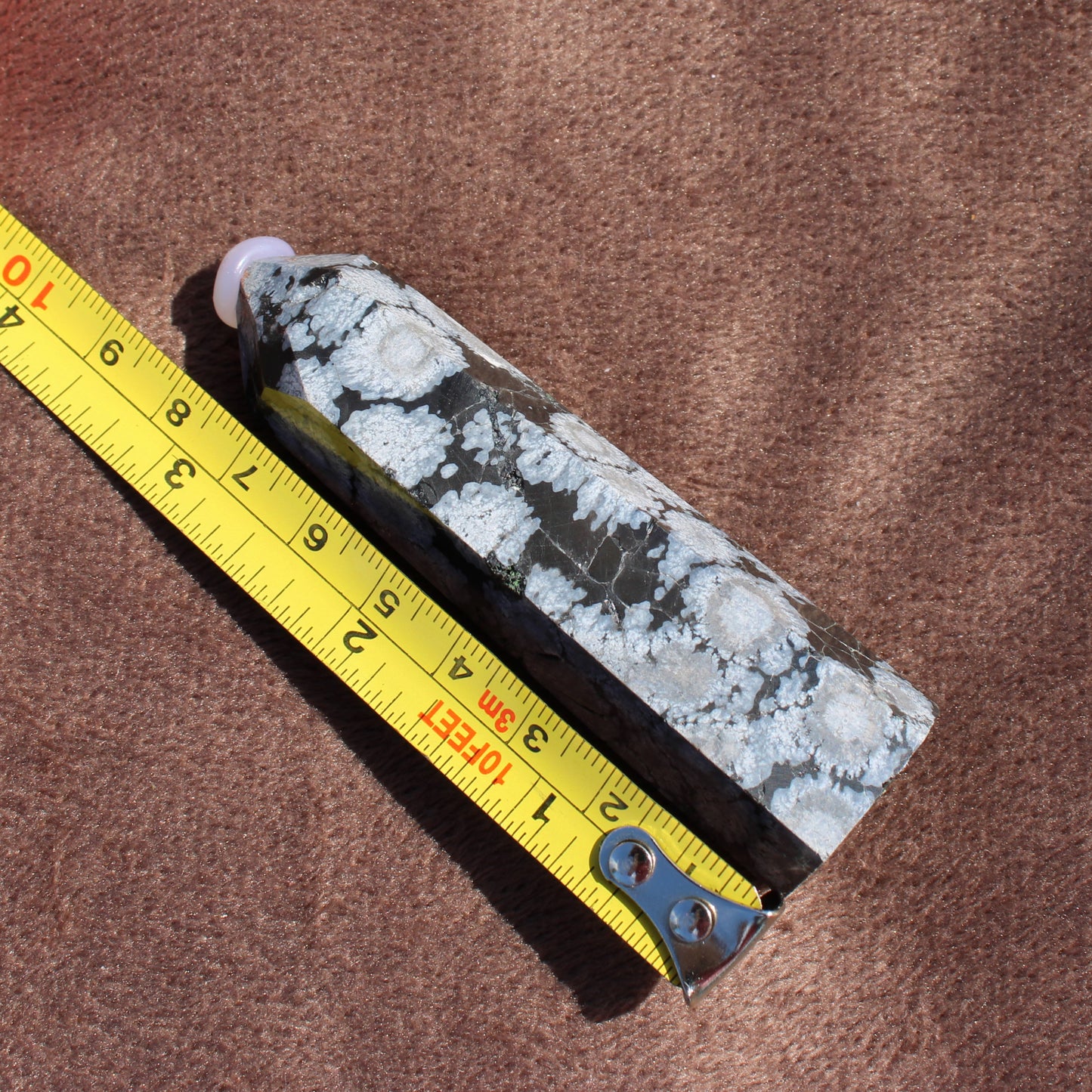 Snowflake Obsidian Tower crystal from Different Branches LLC next to a measuring tape showing size