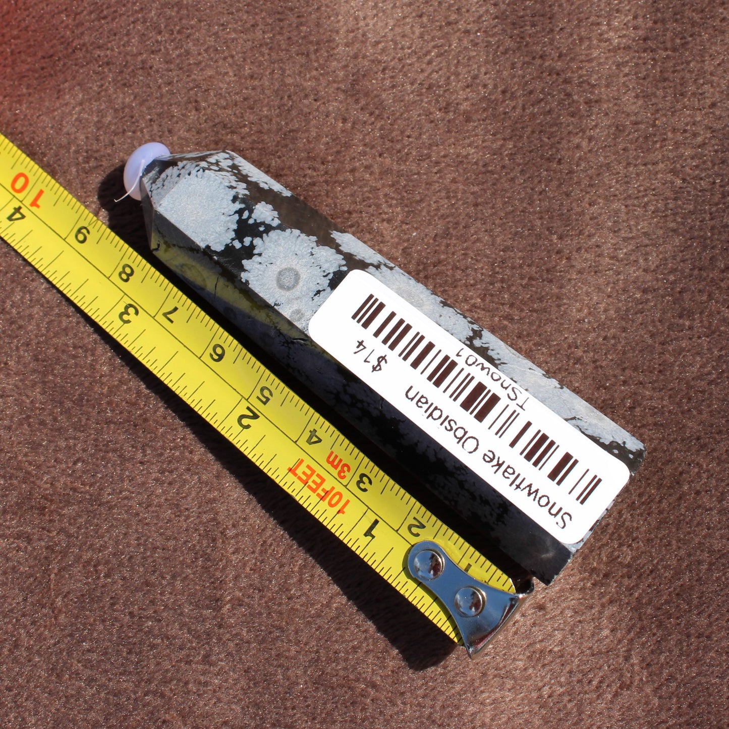 Snowflake Obsidian Tower crystal from Different Branches LLC placed next to a measuring tape on a brown surface