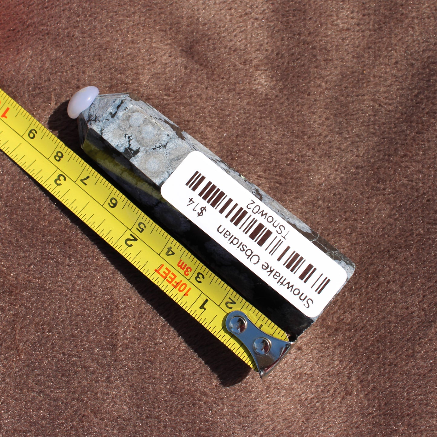 Snowflake Obsidian Tower crystal measuring about 5 inches on a yellow tape from Different Branches LLC