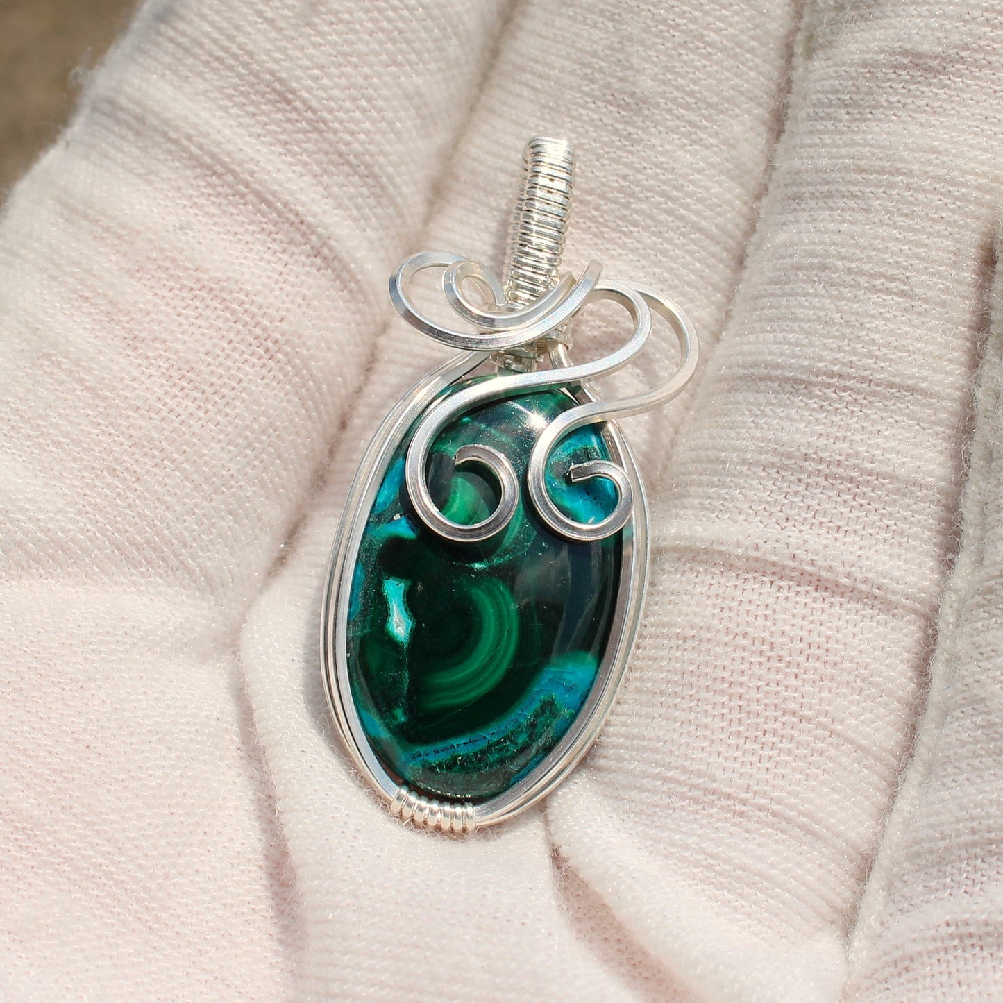Sterling Silver Chrysocolla Malachite pendant with intricate wire wrapping held in a gloved hand