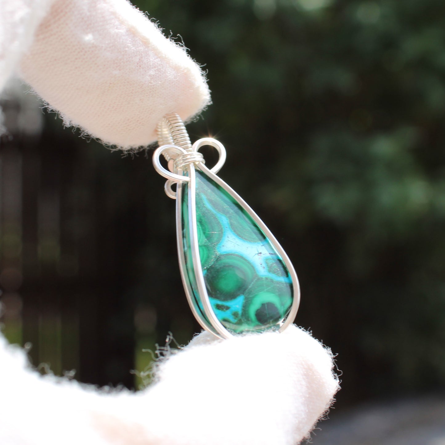 Sterling Silver Chrysocolla Malachite teardrop pendant held by a gloved hand with blurred background