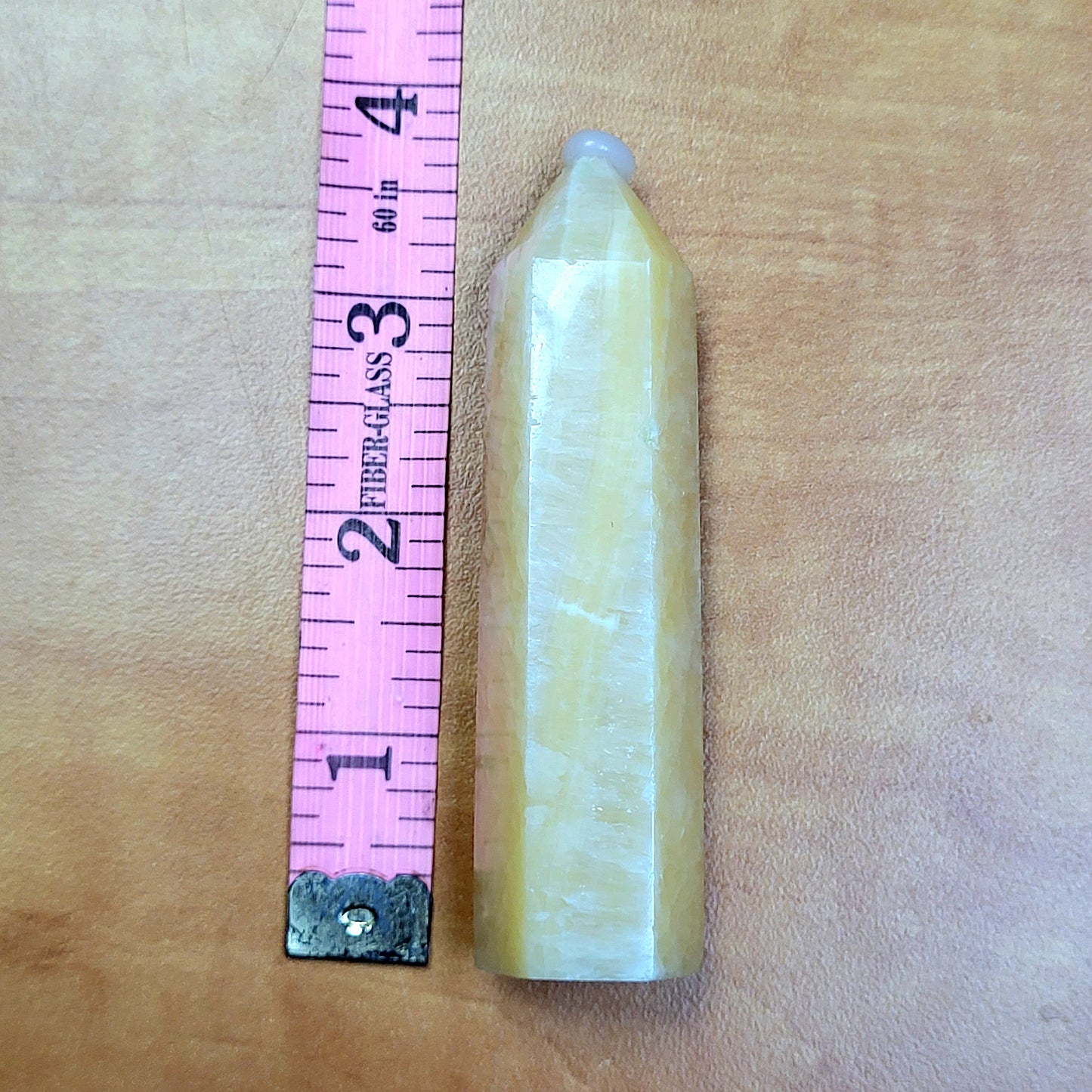 Yellow Calcite Towers crystal with a smooth finish next to a measuring tape for size reference