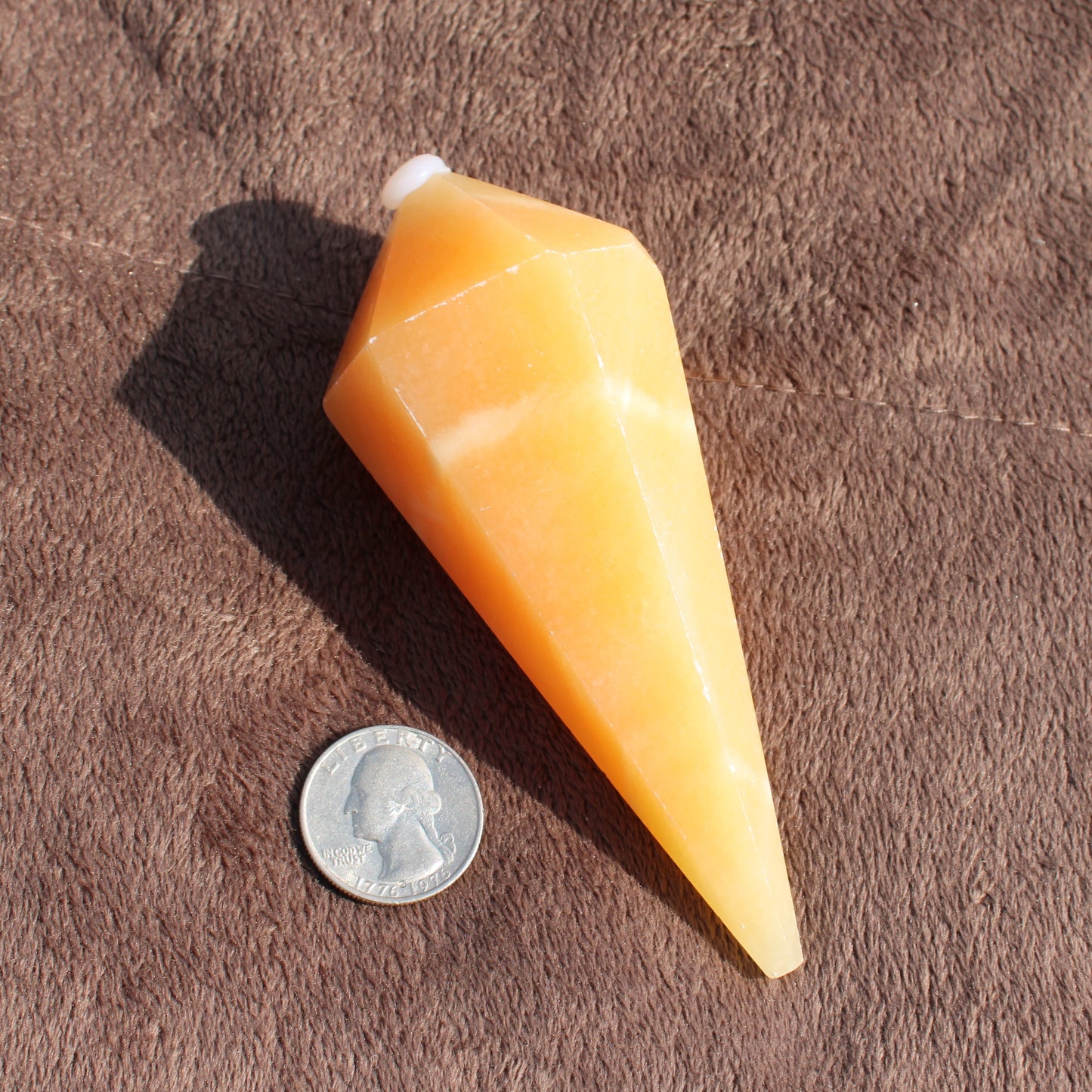 Yellow Calcite Wand crystal with smooth facets next to a US quarter for size comparison on brown fabric