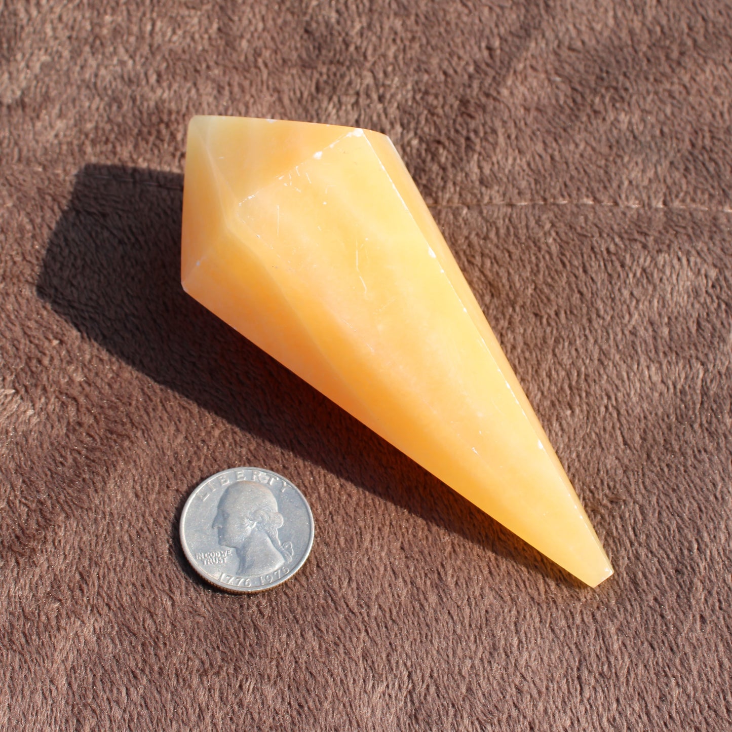 Yellow Calcite Wand crystal next to US quarter for size comparison on brown surface