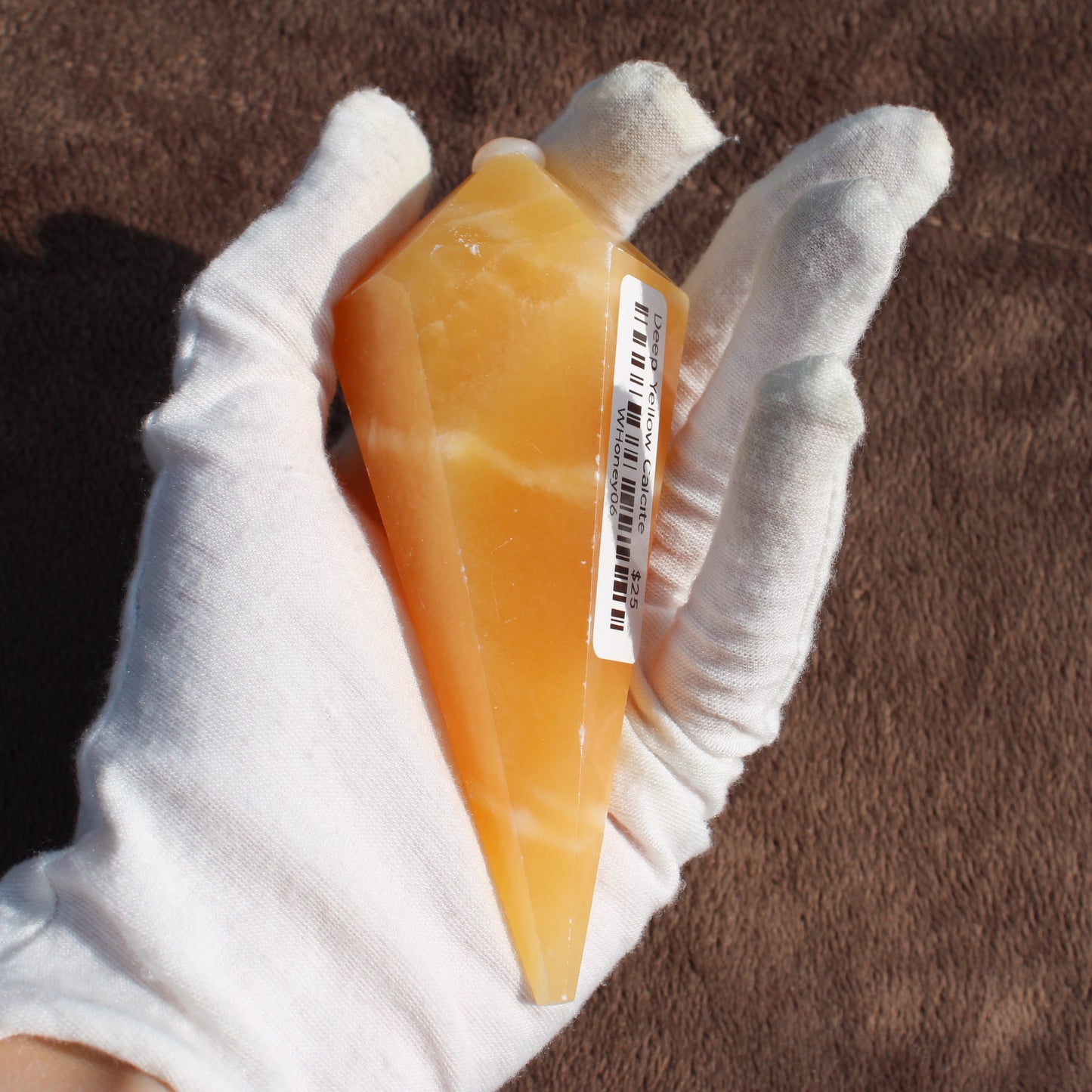 Yellow Calcite Wand crystal held in white gloved hand showing its polished pointed shape