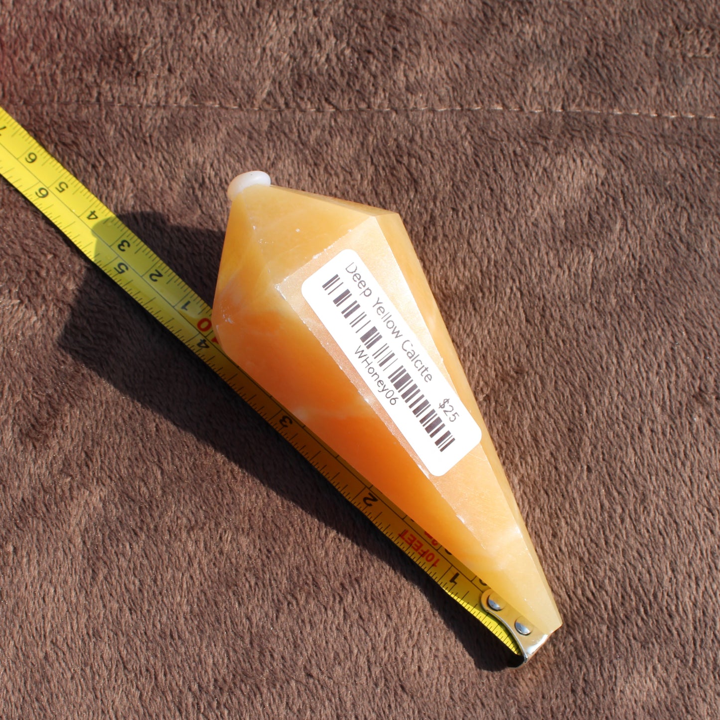 Yellow Calcite Wand crystal from Different Branches LLC shown with measuring tape on brown fabric