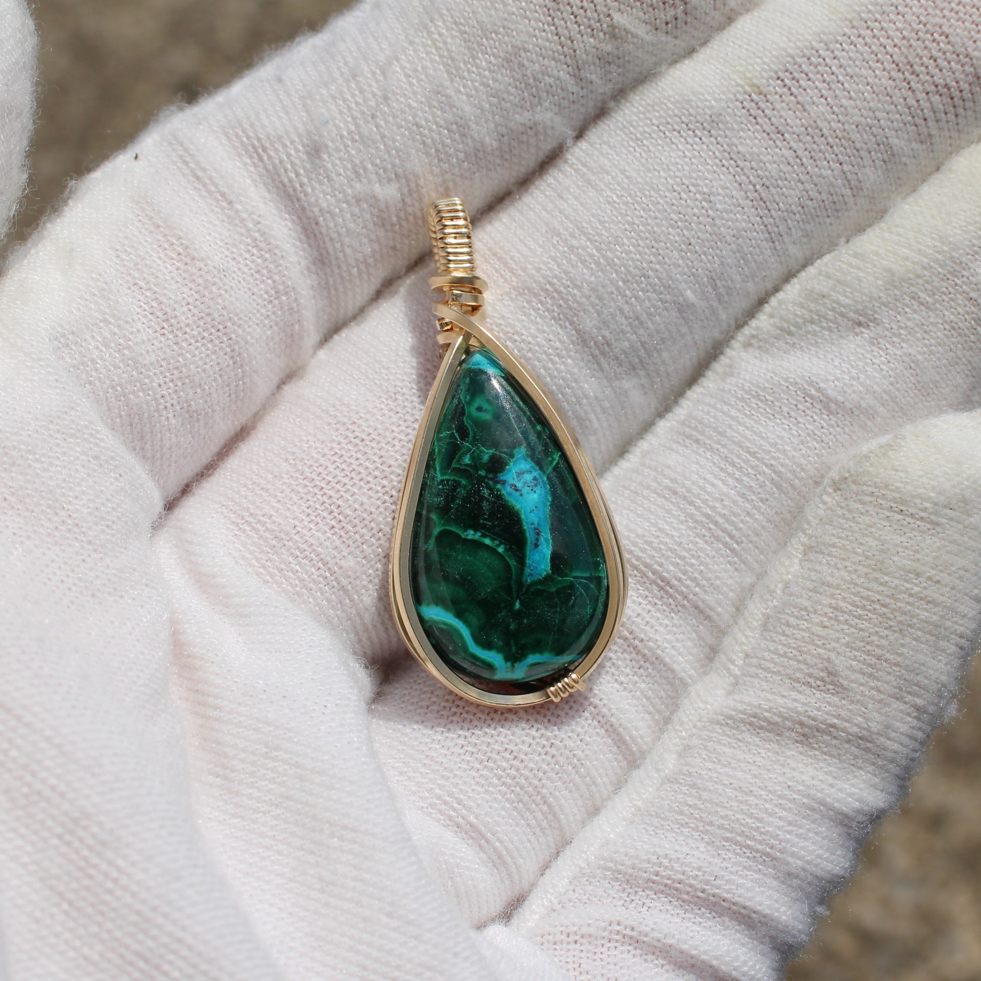 14k Gold Filled Chrysocolla Malachite teardrop pendant held in a white gloved hand