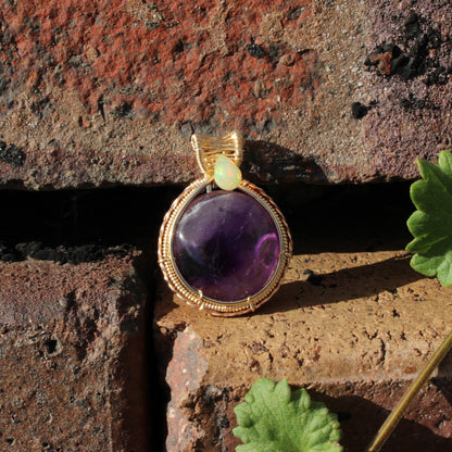 Amethyst Ethiopian Opal 14k yellow and rose gold fill pendant resting on brick with green leaves