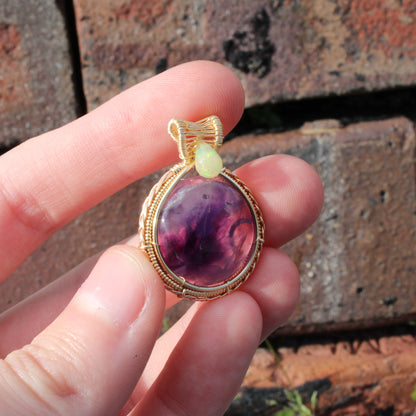 Stunning Amethyst Ethiopian Opal 14k yellow and rose gold fill pendant held in hand against a brick background