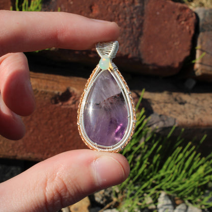 Amethyst & Ethiopian opal sterling silver pendant held between fingers, showcasing its unique design and colors.