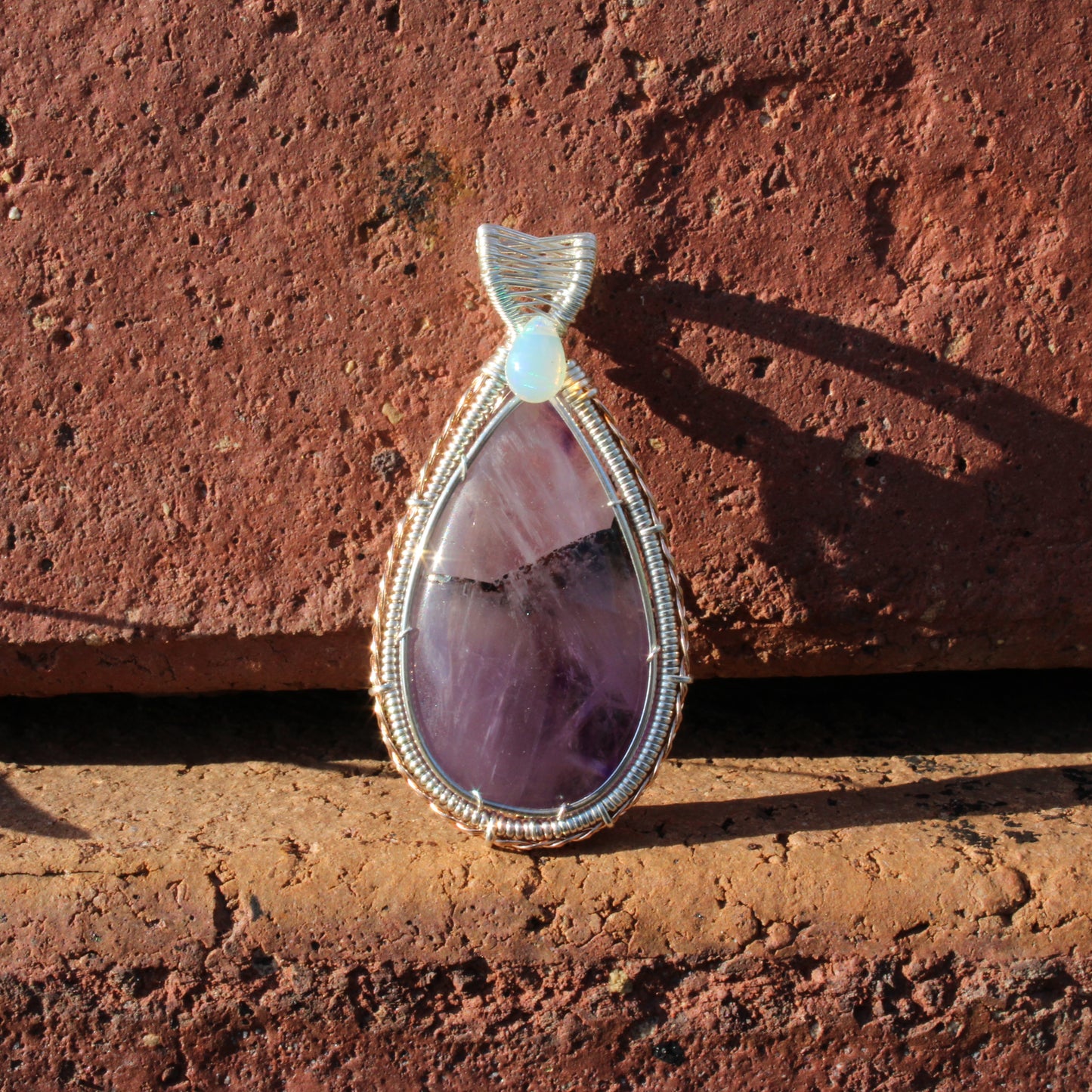 Amethyst & Ethiopian opal sterling silver pendant with intricate wire wrapping design on a rustic background