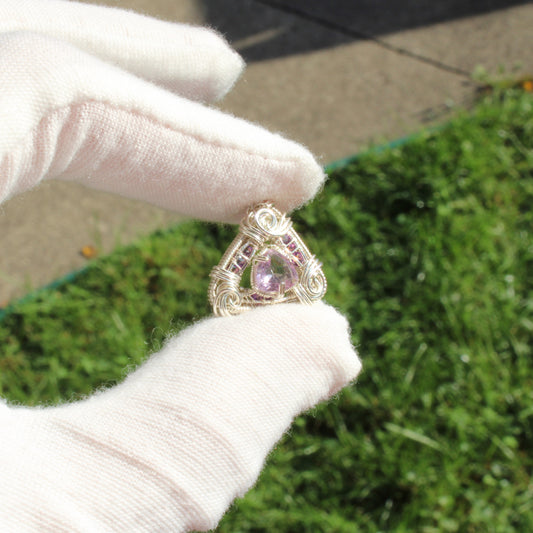 Handcrafted jewelry featuring an Amethyst set in sterling silver pendant held between gloved fingers