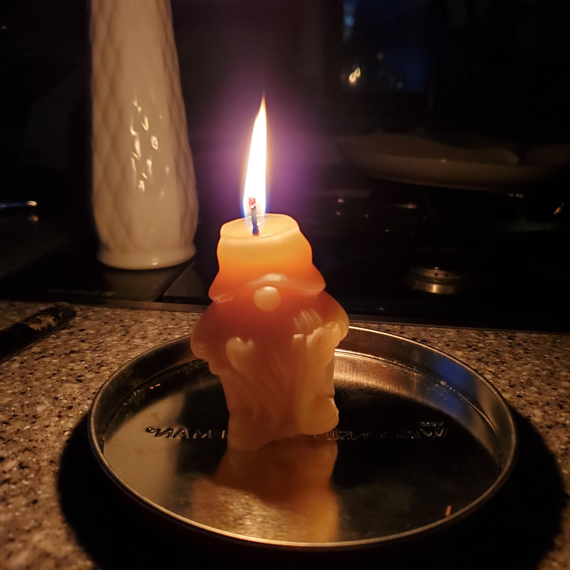 Beeswax gnome candle glowing with a flame on a silver plate in a cozy setting