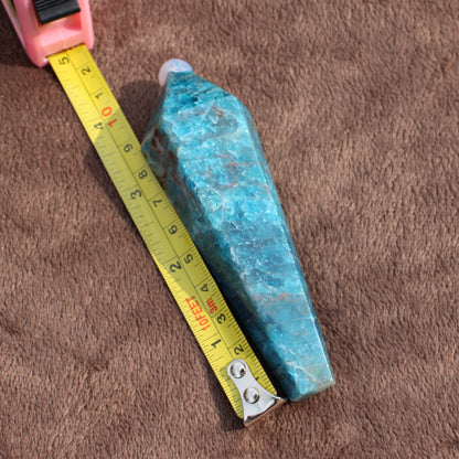 Blue Apatite Wand crystal next to measuring tape on brown fabric showing size and texture