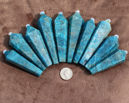 Set of polished Blue Apatite Wand crystals from Different Branches LLC displayed on brown fabric with a quarter for size reference