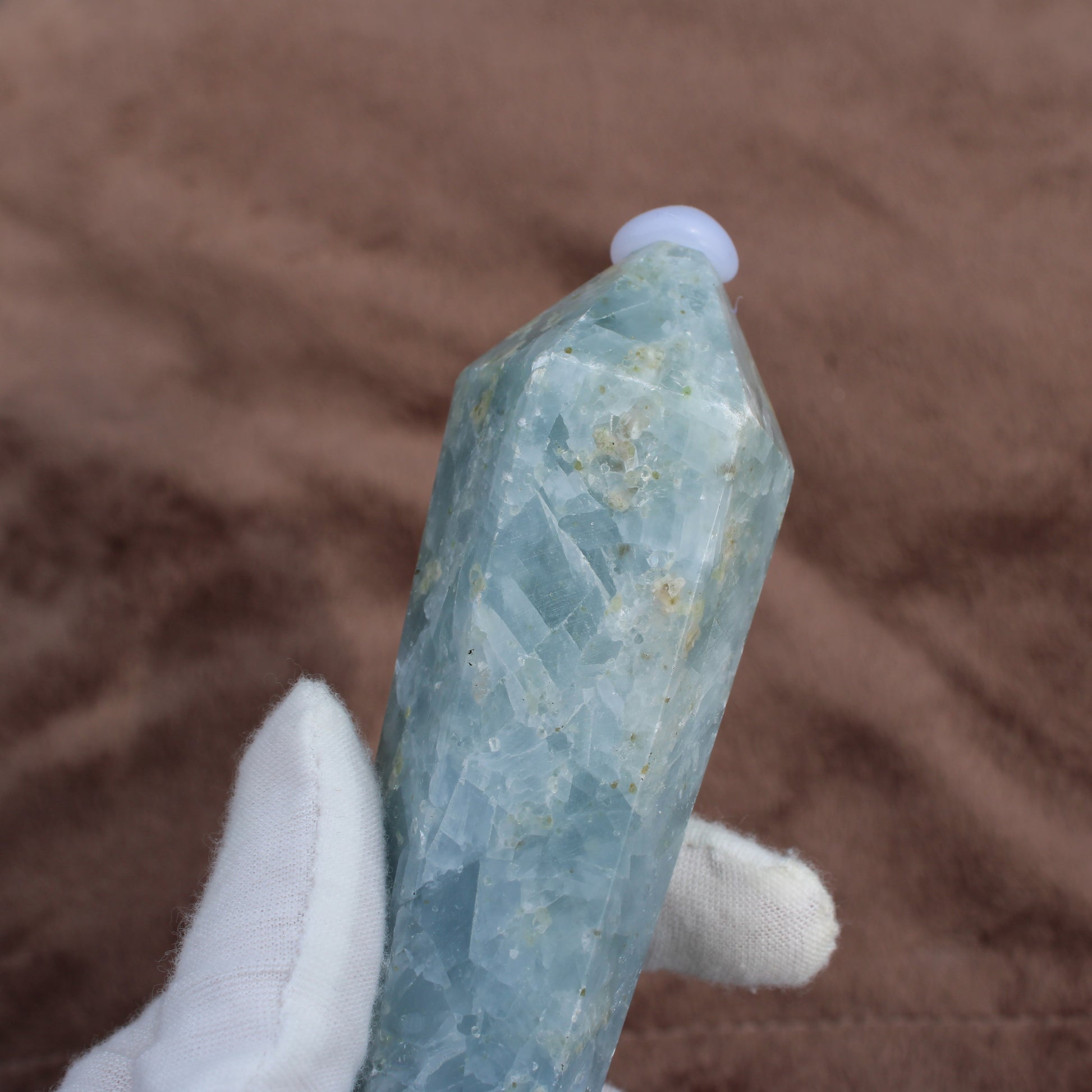 Blue Calcite Wand crystal held in white glove showing its translucent blue tones and natural texture