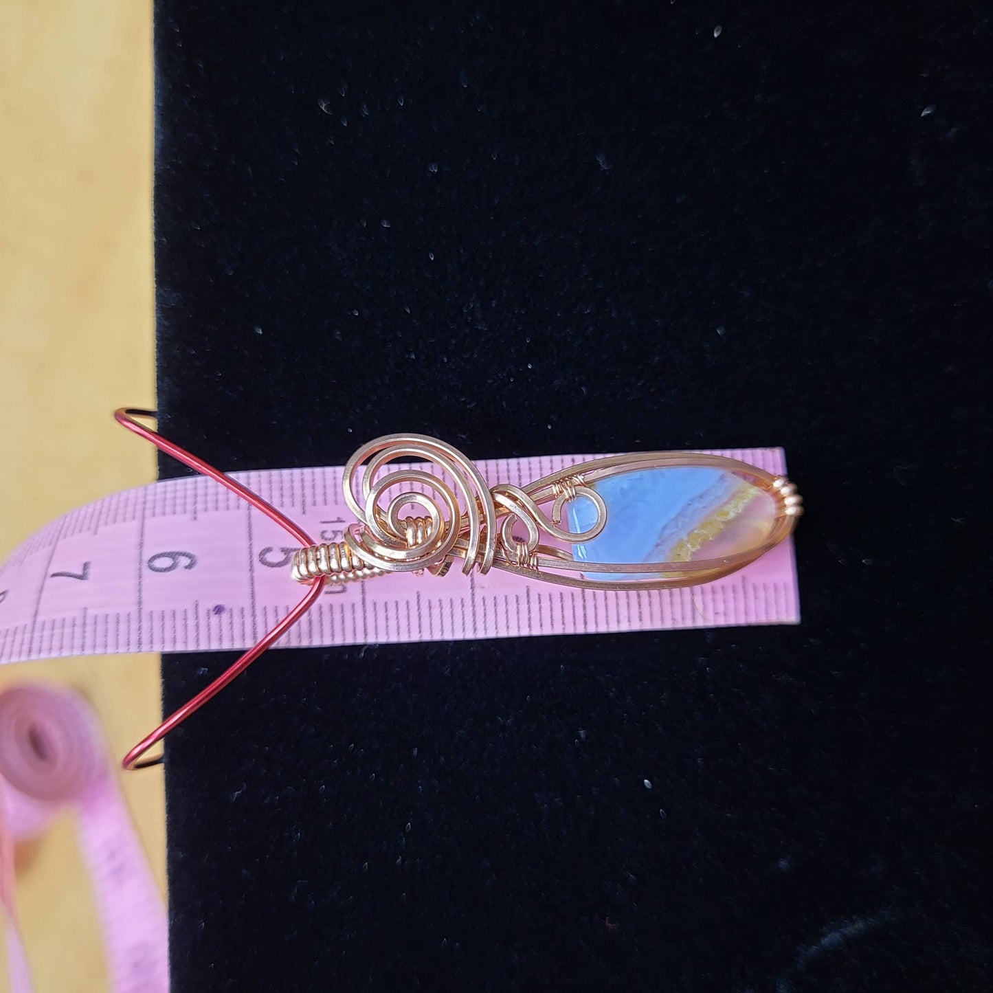 Blue chalcedony pendant wrapped in copper wire with a unique swirl design on a measuring tape