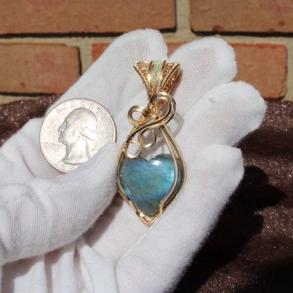 Blue flash labradorite heart pendant with gold accent held next to a quarter for size reference