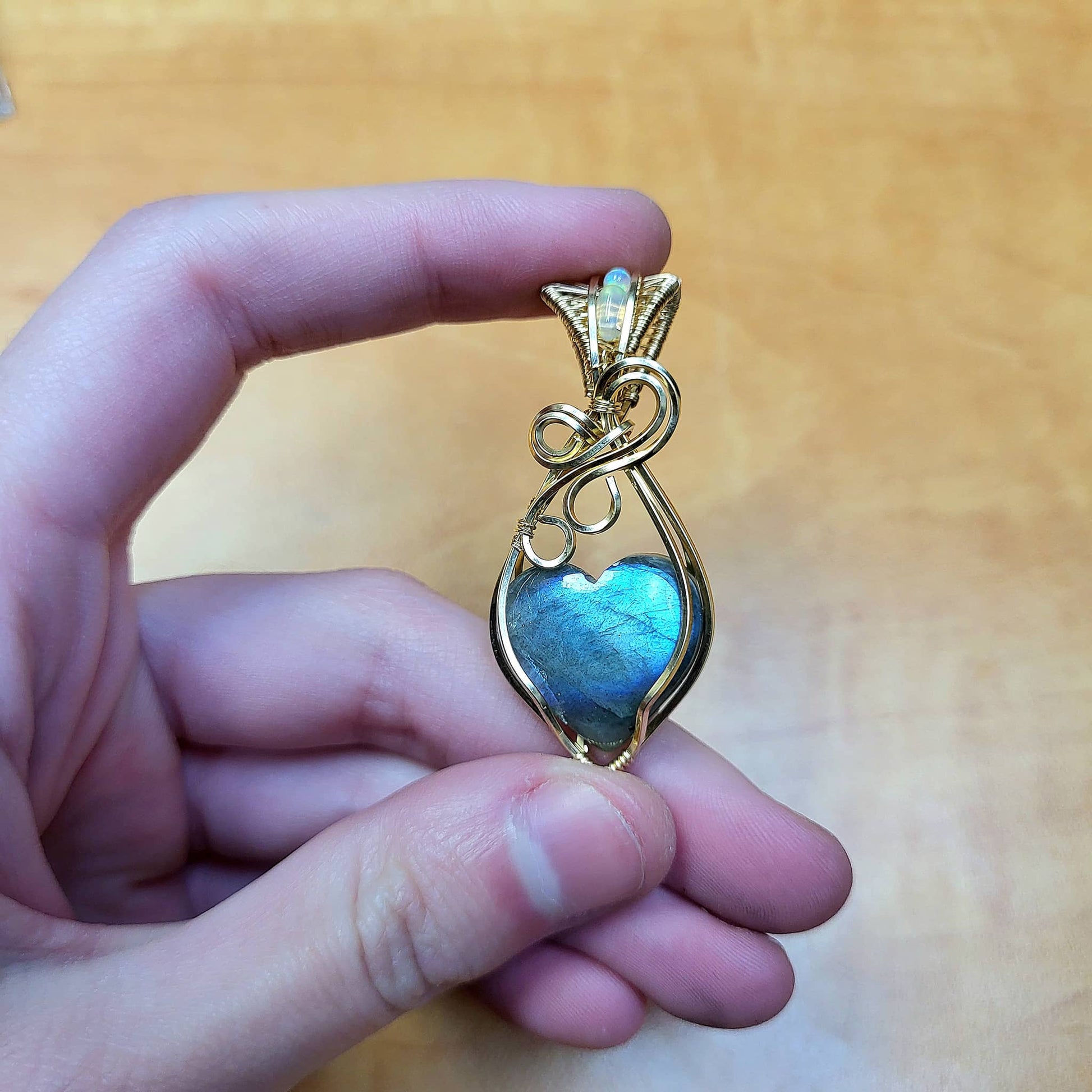 Hand holding a gold love-inspired design pendant featuring a blue flash labradorite heart pendant