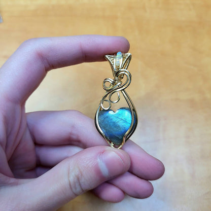 Hand holding a gold love-inspired design pendant featuring a blue flash labradorite heart pendant