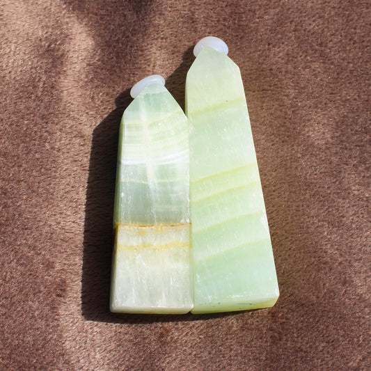 Two polished green and white Calcite Tower crystals by Different Branches LLC on a brown surface