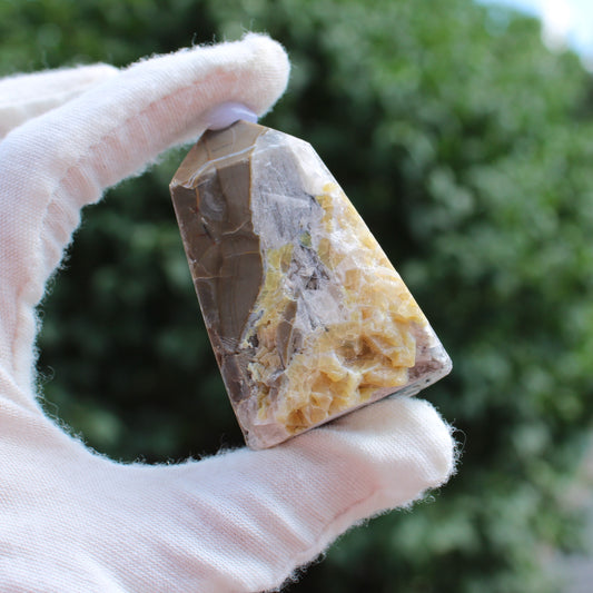 Hand holding a polished Calcite Tower crystal with natural yellow and brown patterns outdoors