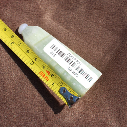 Calcite Tower crystal from Different Branches LLC shown next to measuring tape on brown surface