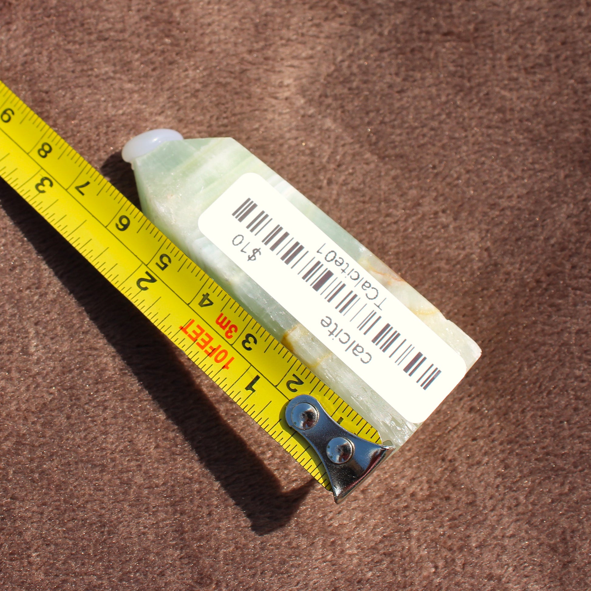 Light green polished Calcite Tower crystal with barcode label next to yellow measuring tape