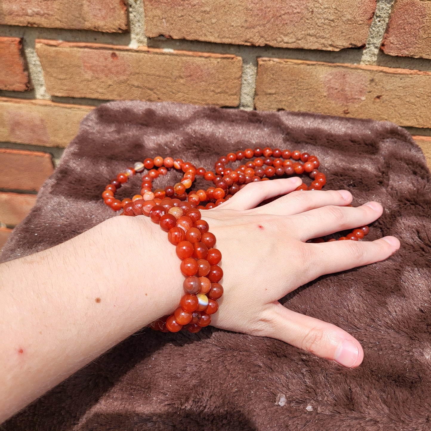 Carnelian bracelet displayed on a hand with a soft fabric background, showcasing vibrant red hues