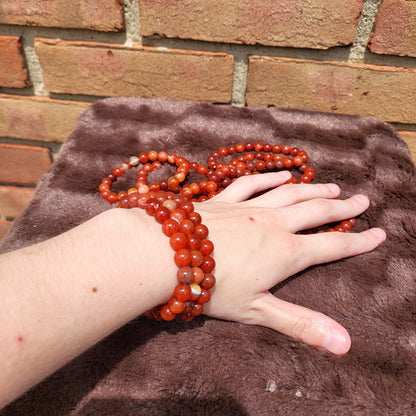 Carnelian bracelet displayed on a hand with a soft fabric background, showcasing vibrant red hues