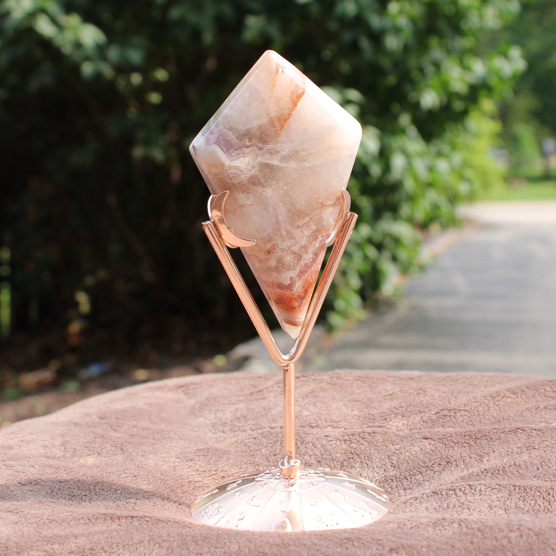 Crazy Lace Agate Diamond crystal in a rose gold stand from Different Branches LLC displayed outdoors