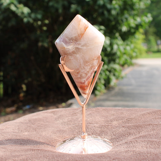 Crazy Lace Agate Diamond crystal in a rose gold stand from Different Branches LLC displayed outdoors