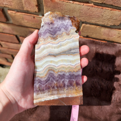 Handheld Crazy lace amethyst slab showcasing unique patterns and vivid colors in natural stone