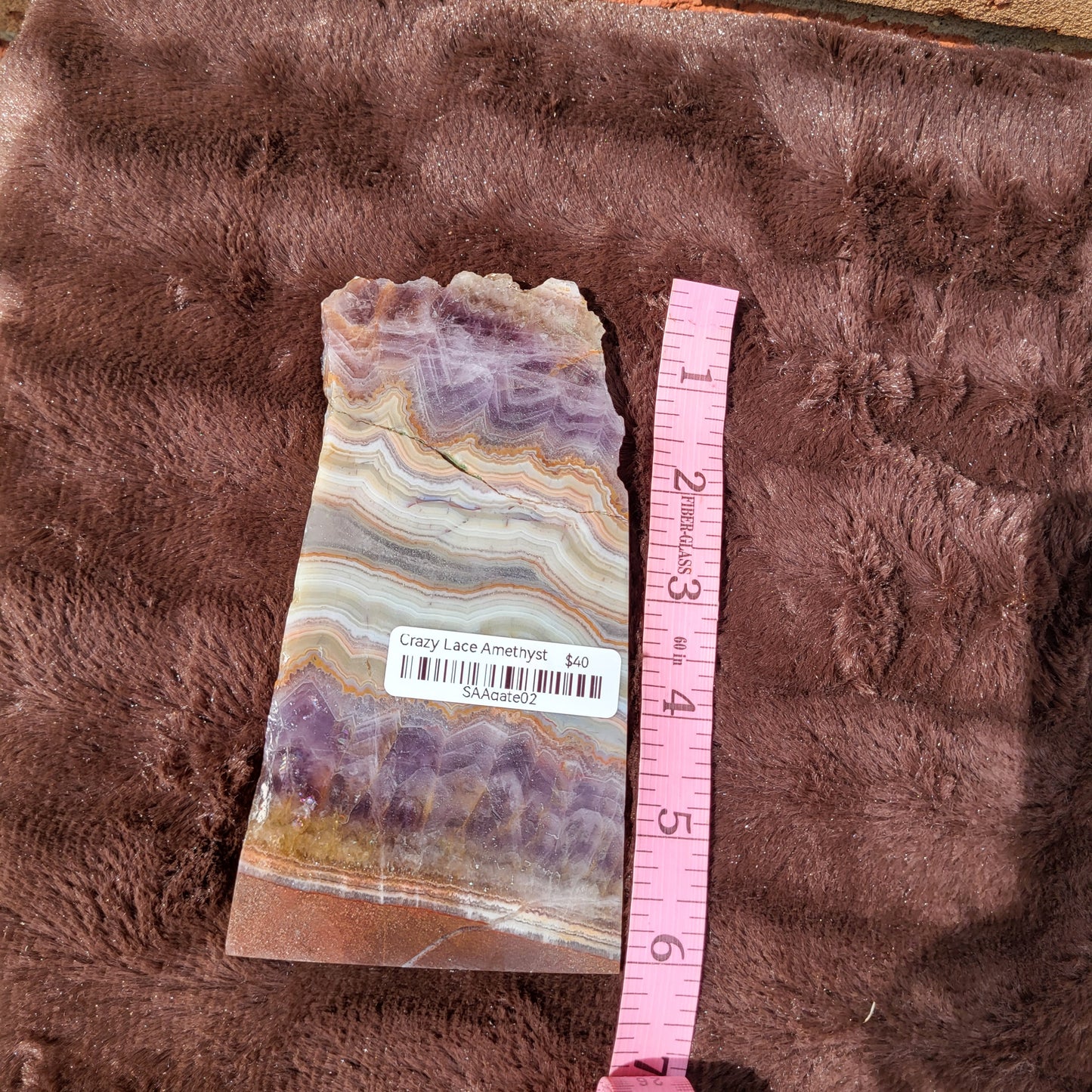 Elegant Crazy lace amethyst slab displayed on soft fabric with a measuring tape for size reference