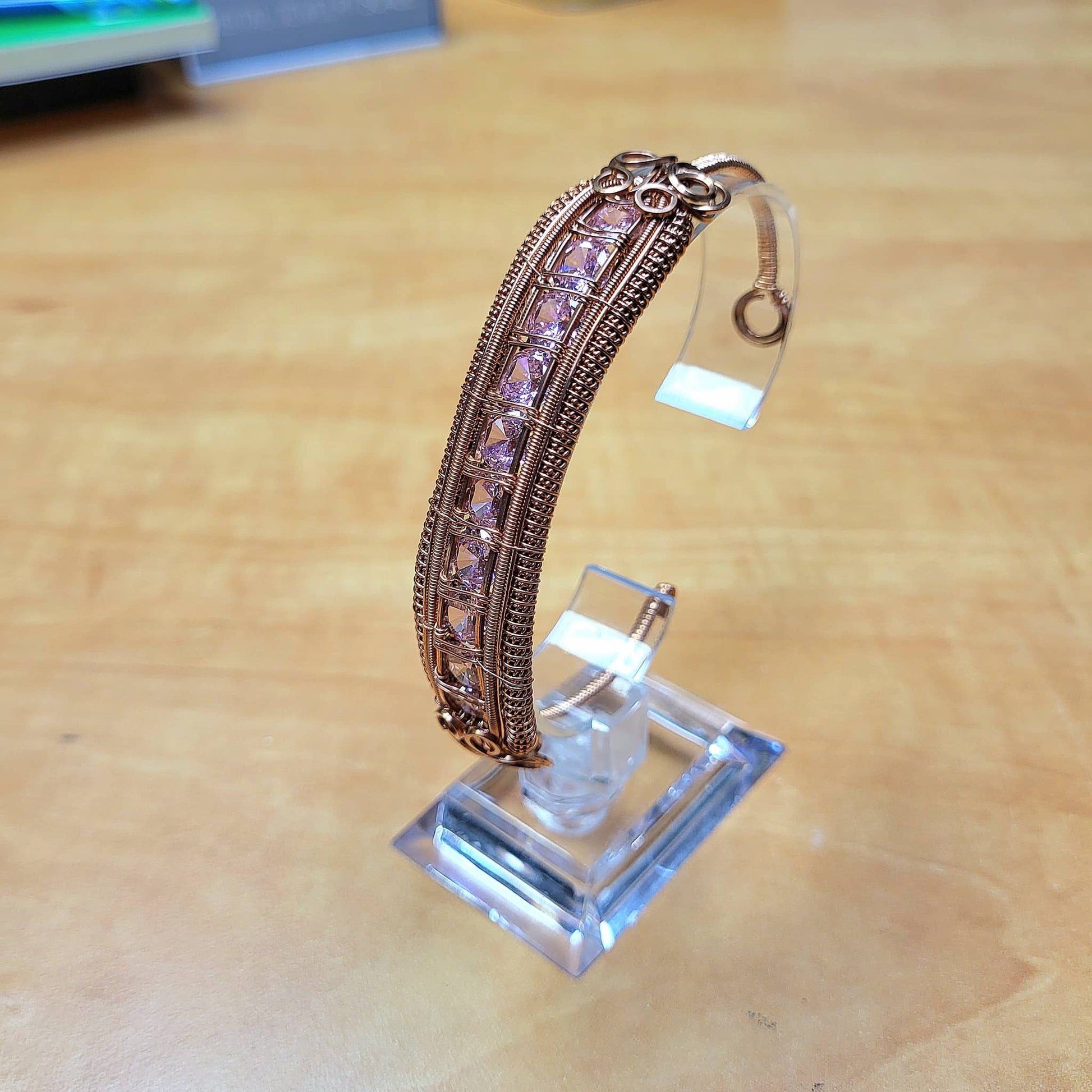 Elegant cubic zirconia bracelet set in a detailed bronze design displayed on a clear stand