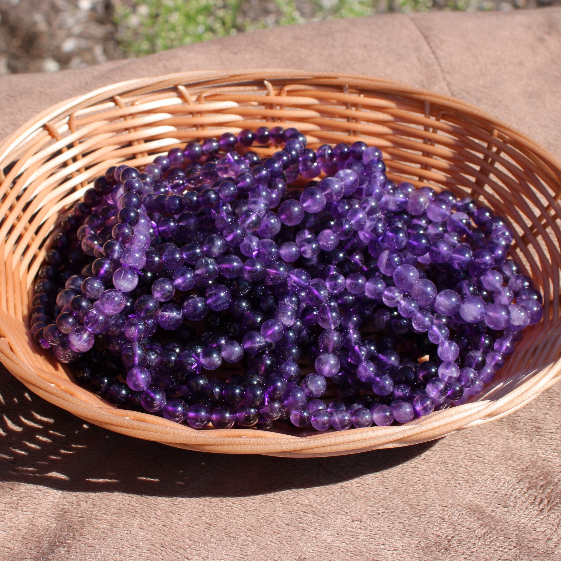 Deep Purple Amethyst Bracelet strands arranged in a woven basket on a sunny surface