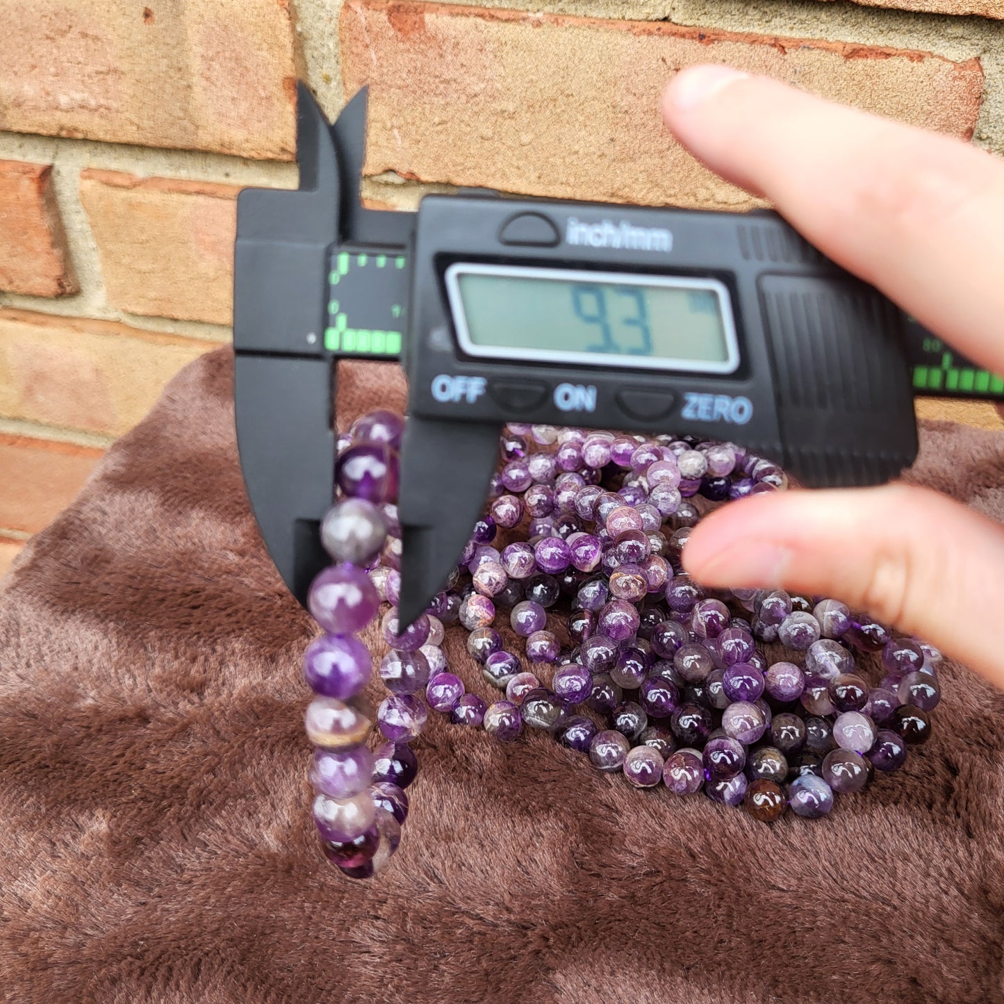 Measuring a Dream Amethyst bracelet with calipers for accurate sizing in a crystal gift shop