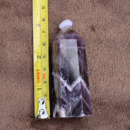 Dream Amethyst Tower crystal standing next to a measuring tape showing size on a brown fabric background