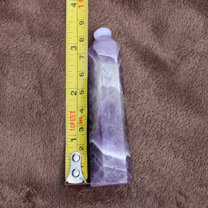 Dream Amethyst Tower crystal measuring about 4 inches placed next to a yellow measuring tape on brown fabric