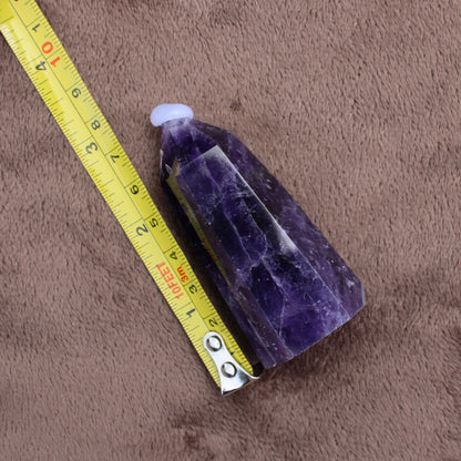 Dream Amethyst Tower crystal measuring about 3 inches next to a yellow tape measure on brown fabric