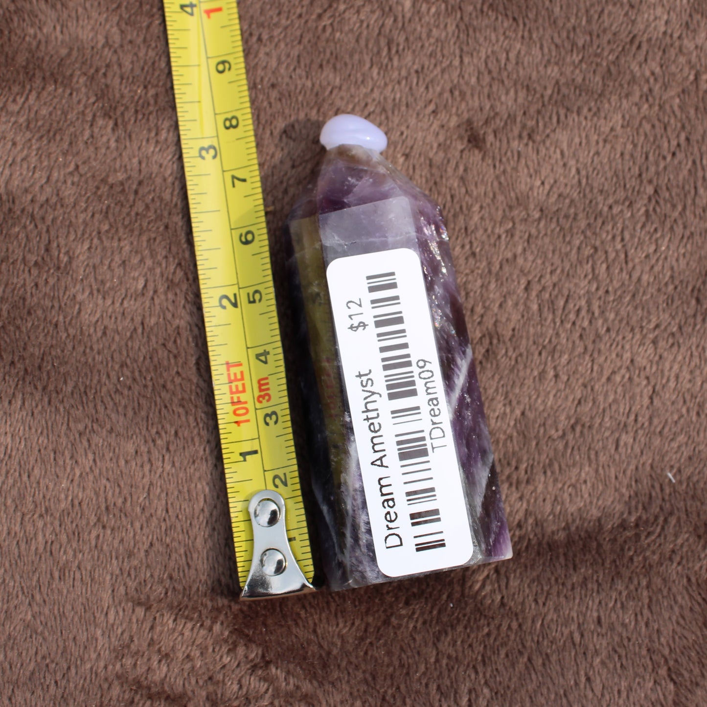 Dream Amethyst Tower crystal with price tag and measuring tape on brown fabric background