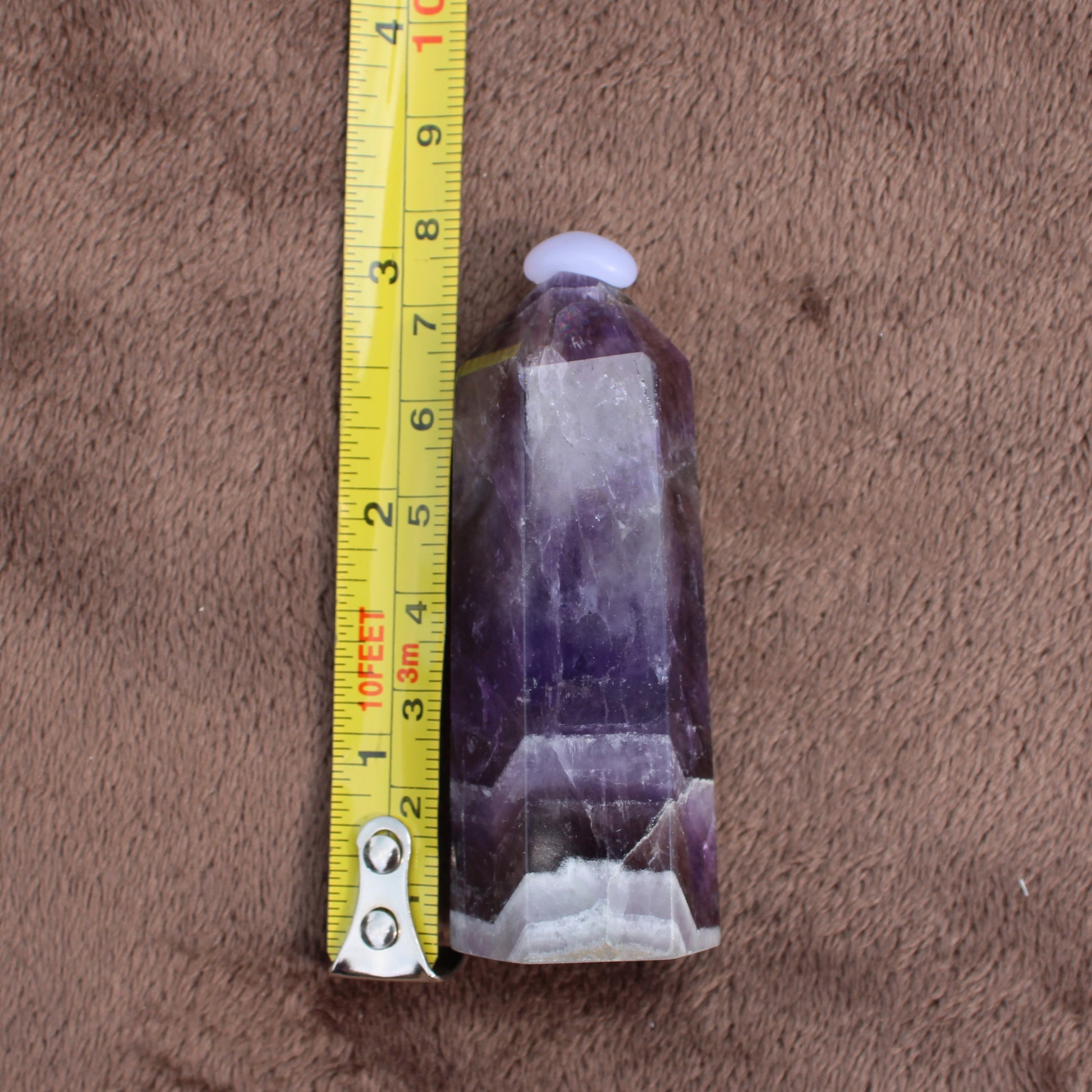 Dream Amethyst Tower crystal standing next to a measuring tape showing size on brown fabric background