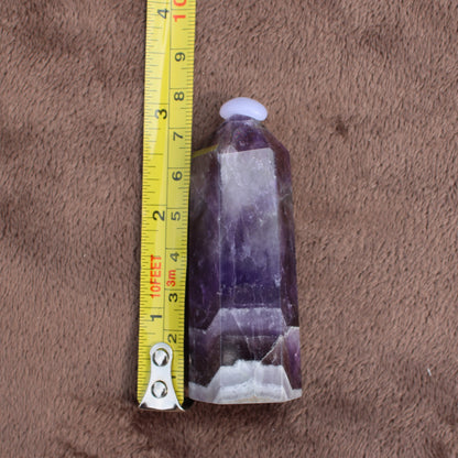 Dream Amethyst Tower crystal standing next to a measuring tape showing size on brown fabric background