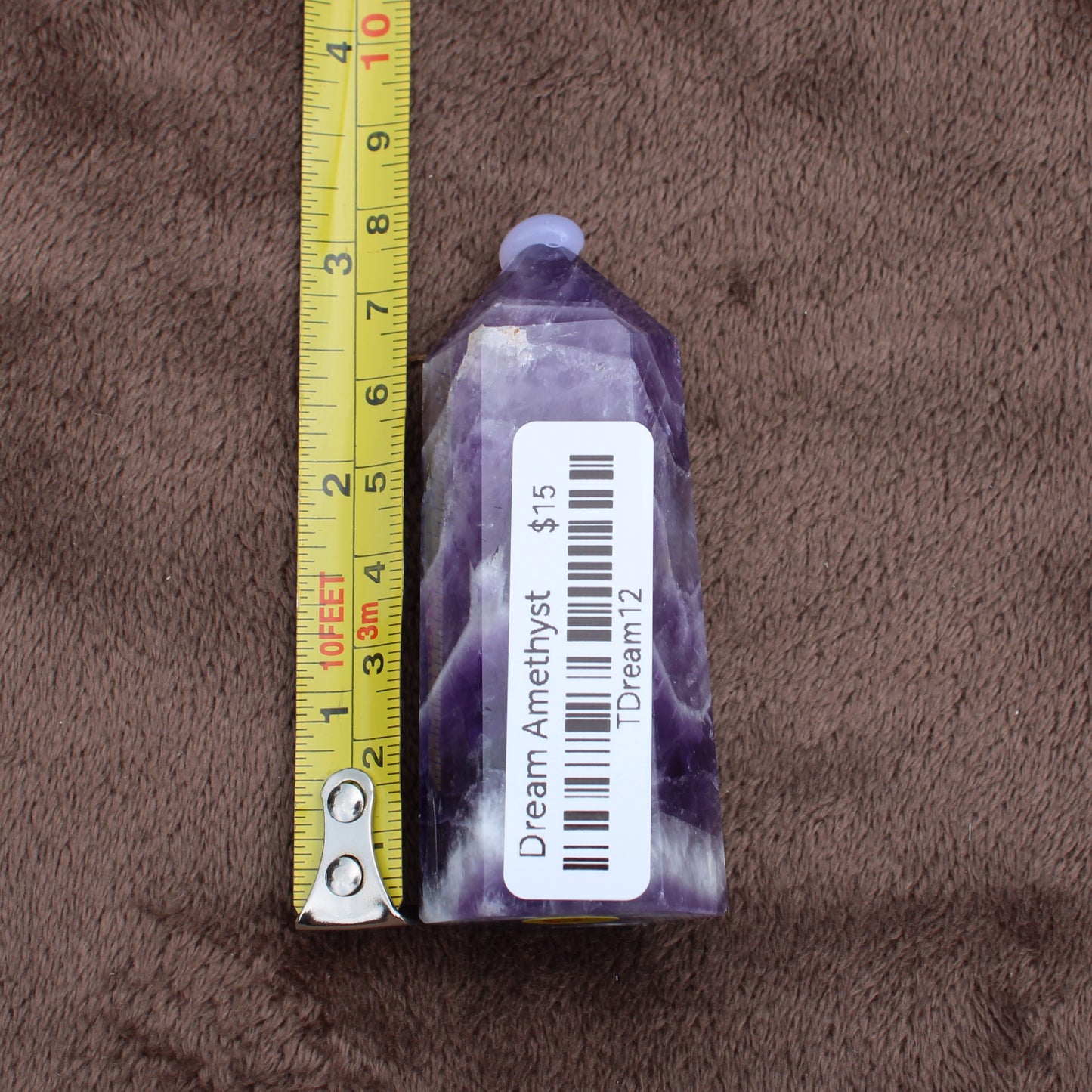 Dream Amethyst Tower crystal with purple and white hues beside a measuring tape showing its size